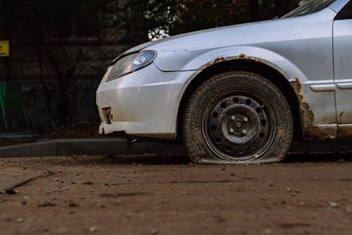 A car with a flat tire parked on the side of a dimly lit road, with emergency lights on.