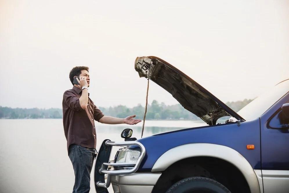 An image of a man calling for help while his car is facing trouble on the road