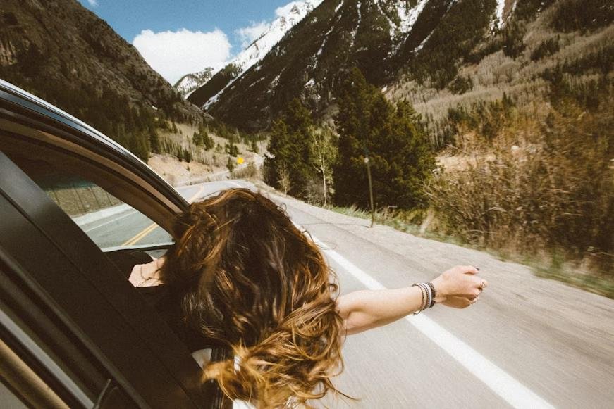 a woman putting her hand outside the window from her car on a road